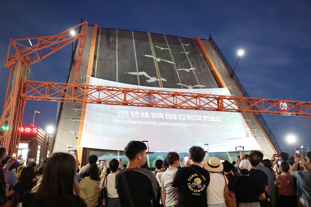 Am 25. Juli schauen sich Besucher bei der Veranstaltung „2026 Busan Wartime Capital Heritage Night” auf der Yeongdo-Brücke in Jung-gu, Busan, ein Video über die 1.023-tägige Geschichte von Busan als Kriegshauptstadt an. Die Brücke ist ein Wahrzeichen von Busan, da sie während des Koreakriegs für zahlreiche Flüchtlinge zu einem Ort des Abschieds und des Wiedersehens wurde.