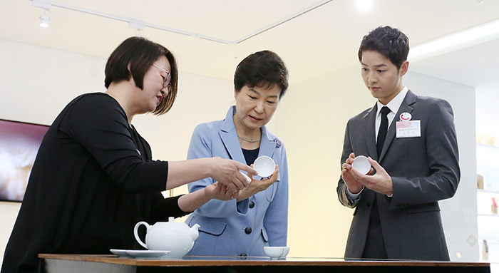 Präsidentin Park Geun-hye (Mitte) hört sich die Erläuterungen von Kim Hye-young (links) an, einer der Unternehmerinnen an der Culture and Creativity Academy, einer Schulungseinrichtung, die junge Talente ausbilden soll. Sie zeigt einen hochwertigen Teetisch, der mit Sensoren ausgestattet ist, die die Temperatur von Tee regulieren können.